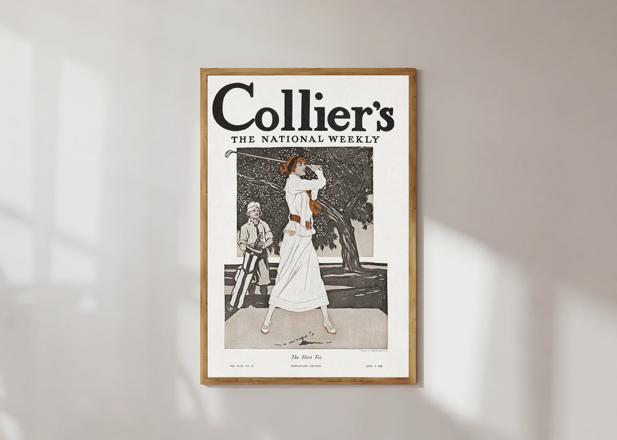 Framed art print of Lady Golfer (The First Tee) by Edward Penfield, in a light wood frame on a sunlit white wall