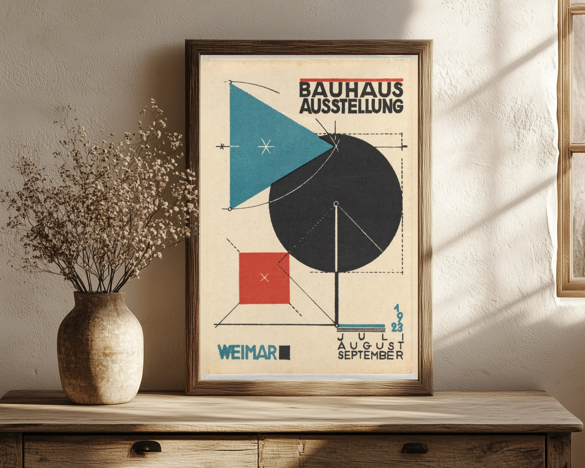 Framed art print of Ausstellung Poster by Bauhaus, in a dark wood frame leaning on a rustic console beside dried flowers