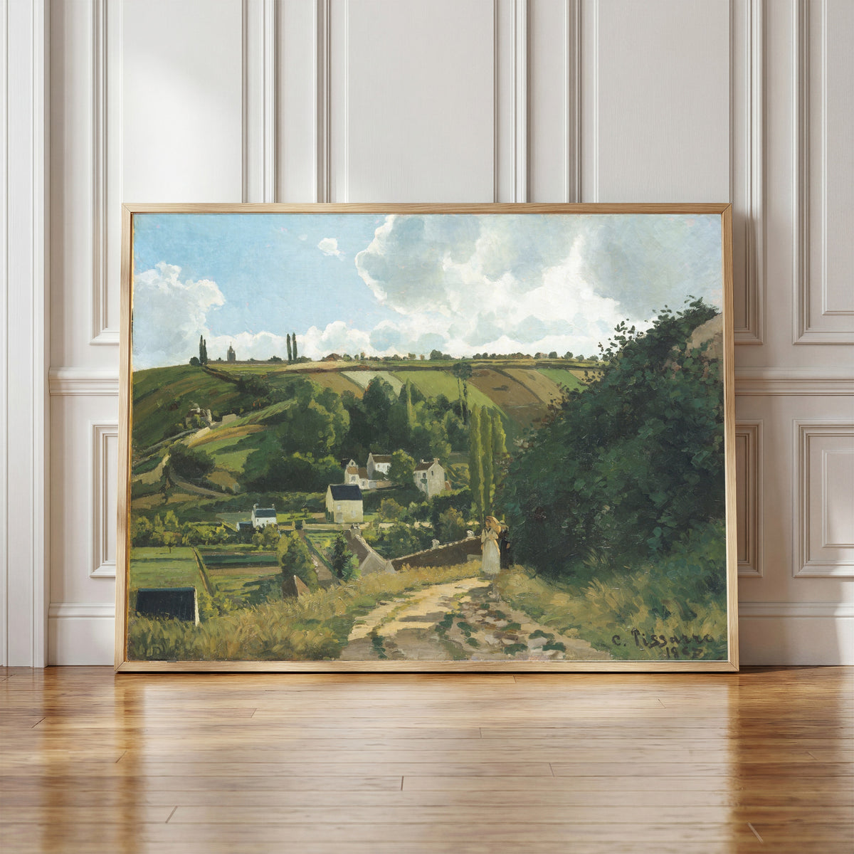 Framed art print of Jalais Hill, Pontoise by Camille Pissarro, in a light wood frame leaning against a panelled white wall