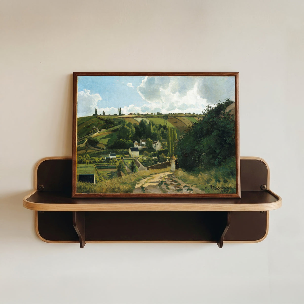 Framed art print of Jalais Hill, Pontoise by Camille Pissarro, in a dark wood frame resting on a wall shelf