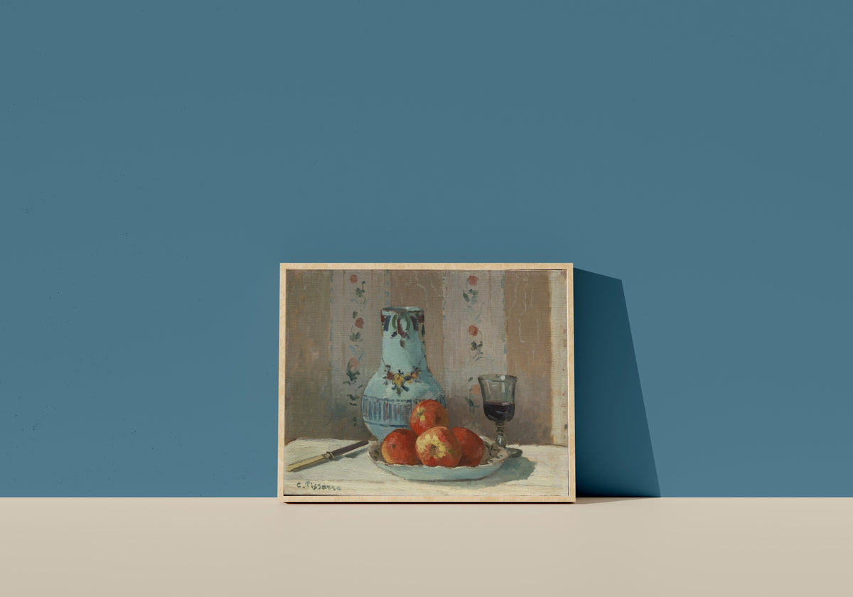 Framed art print of Still Life with Apples and Pitcher by Camille Pissarro, in a light wood frame leaning on a blue wall