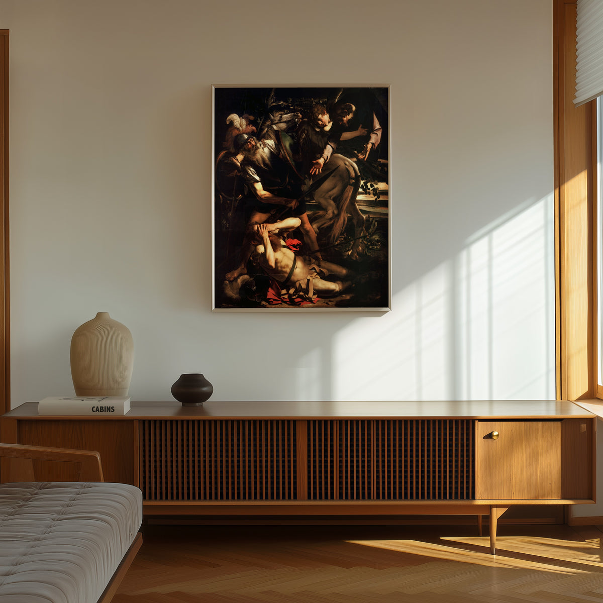 Framed art print of Conversion of St. Paul by Caravaggio, in a thin light frame on a sunlit wall above a wooden sideboard