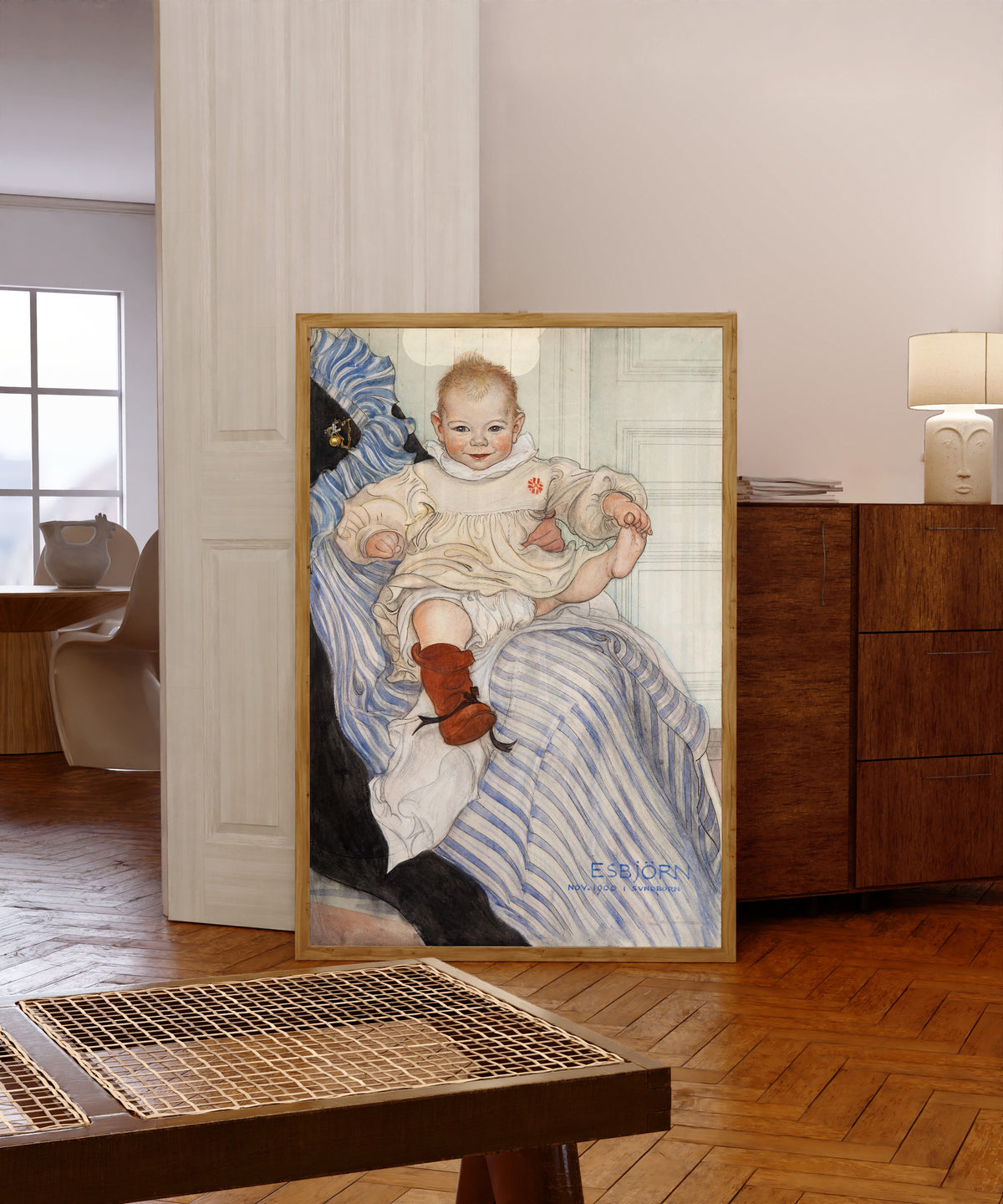Framed art print of Esbjörn by Carl Larsson, in a light wood frame leaning in a warm room with a parquet floor