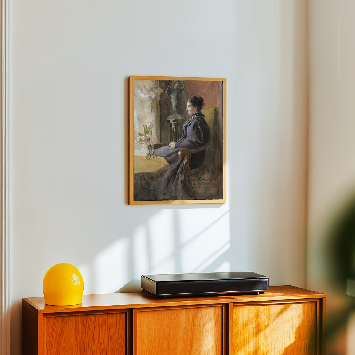 Framed art print of Eva Upmark, née Kindstrand by Carl Larsson, in a light wood frame on a white wall above an orange sideboard