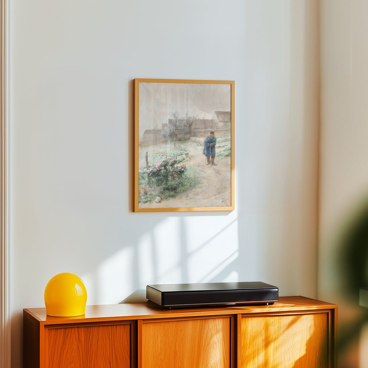 Framed art print of November by Carl Larsson, in a light wood frame on a white wall above an orange sideboard