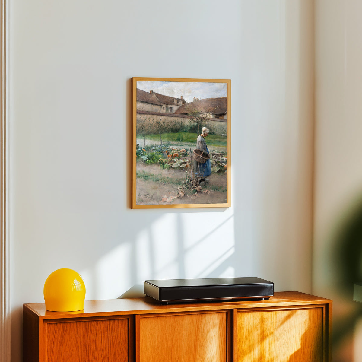 Framed art print of October by Carl Larsson, in a light wood frame on a white wall above an orange sideboard