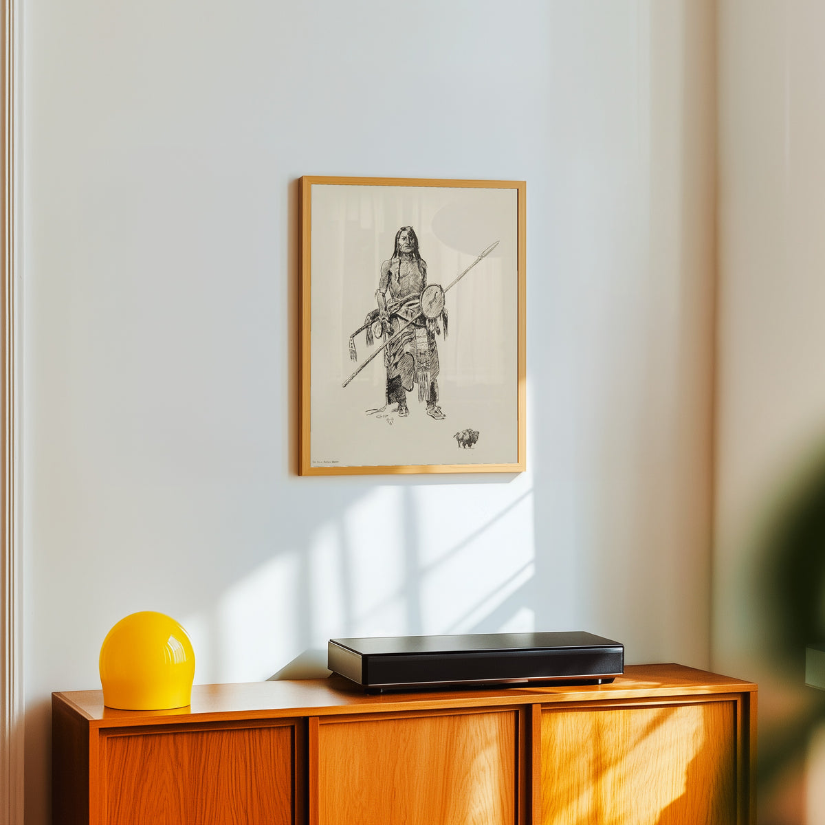 Framed art print of The Sioux Buffalo Hunter by Charles M. Russell, in a light wood frame on a white wall above an orange sideboard