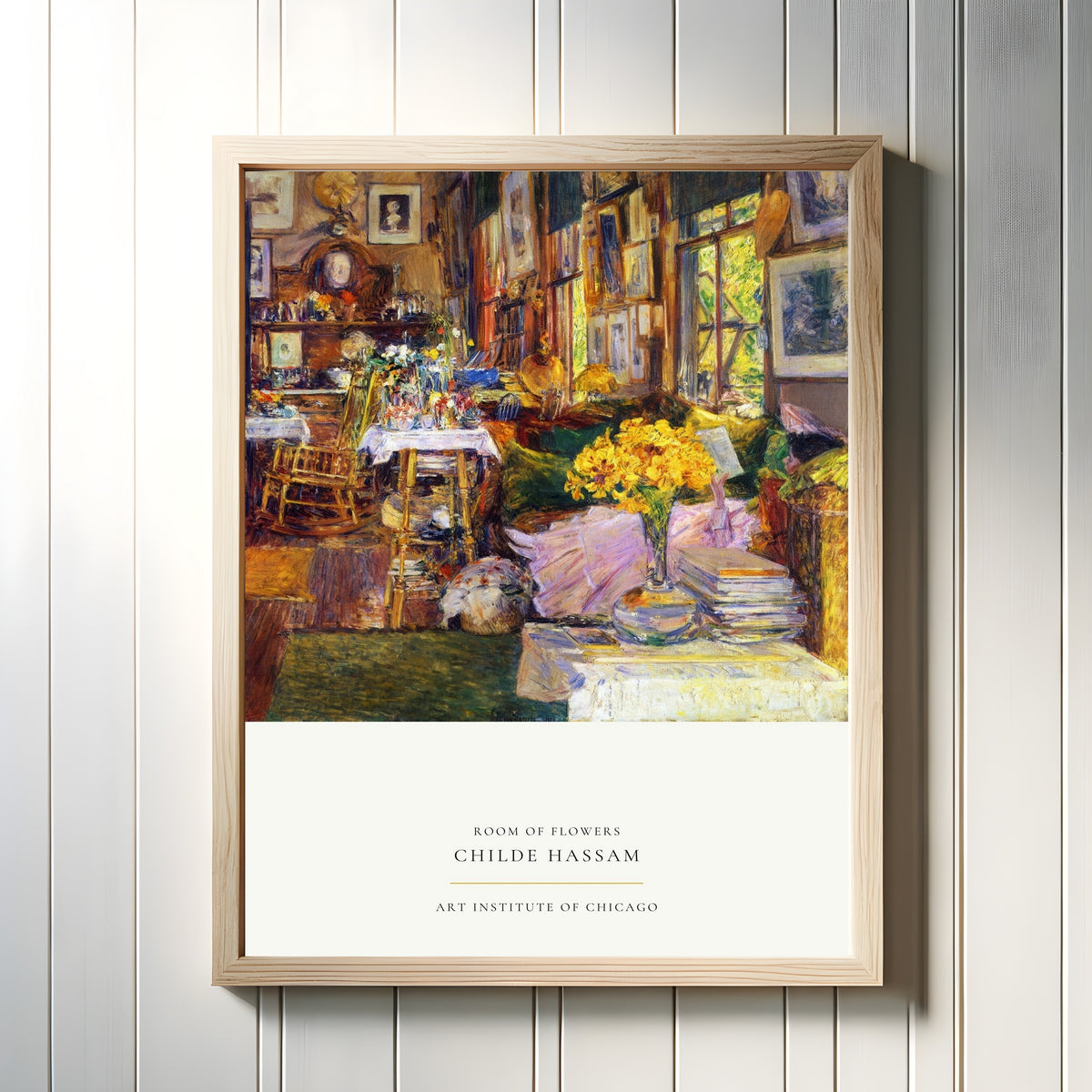 Framed art print of Room of Flowers by Childe Hassam, in a light wood frame on a white panelled wall