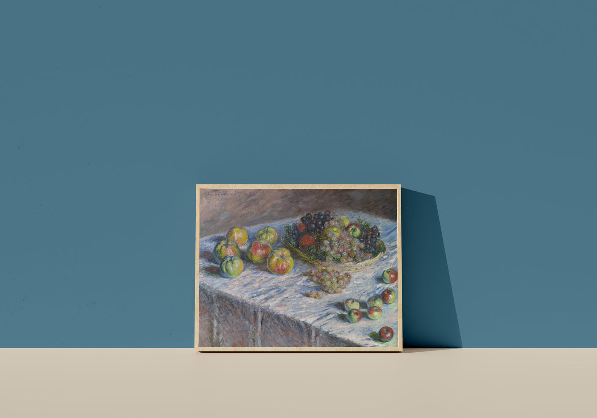 Framed art print of Apples and Grapes by Claude Monet, in a light wood frame leaning on a blue wall