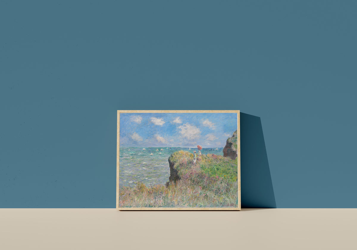 Framed art print of Cliff Walk at Pourville by Claude Monet, in a light wood frame leaning on a blue wall