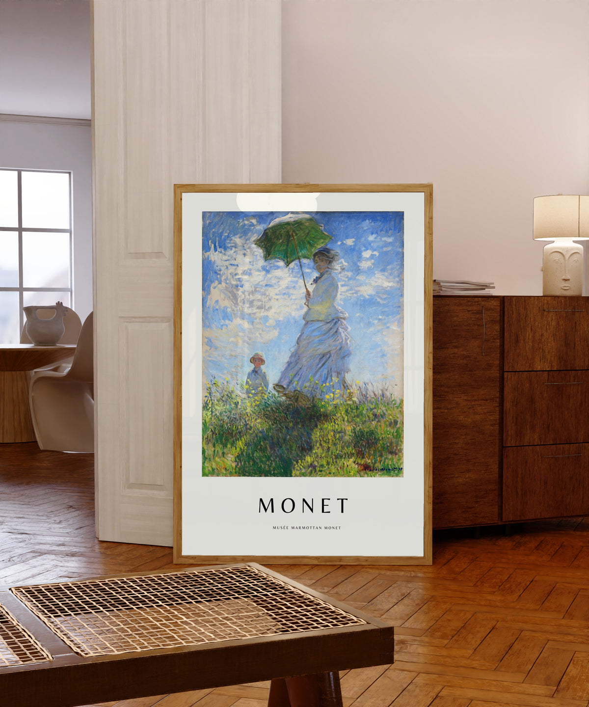 Framed art print of Madame Monet with a Parasol by Claude Monet, in a light wood frame leaning in a warm room with a parquet floor