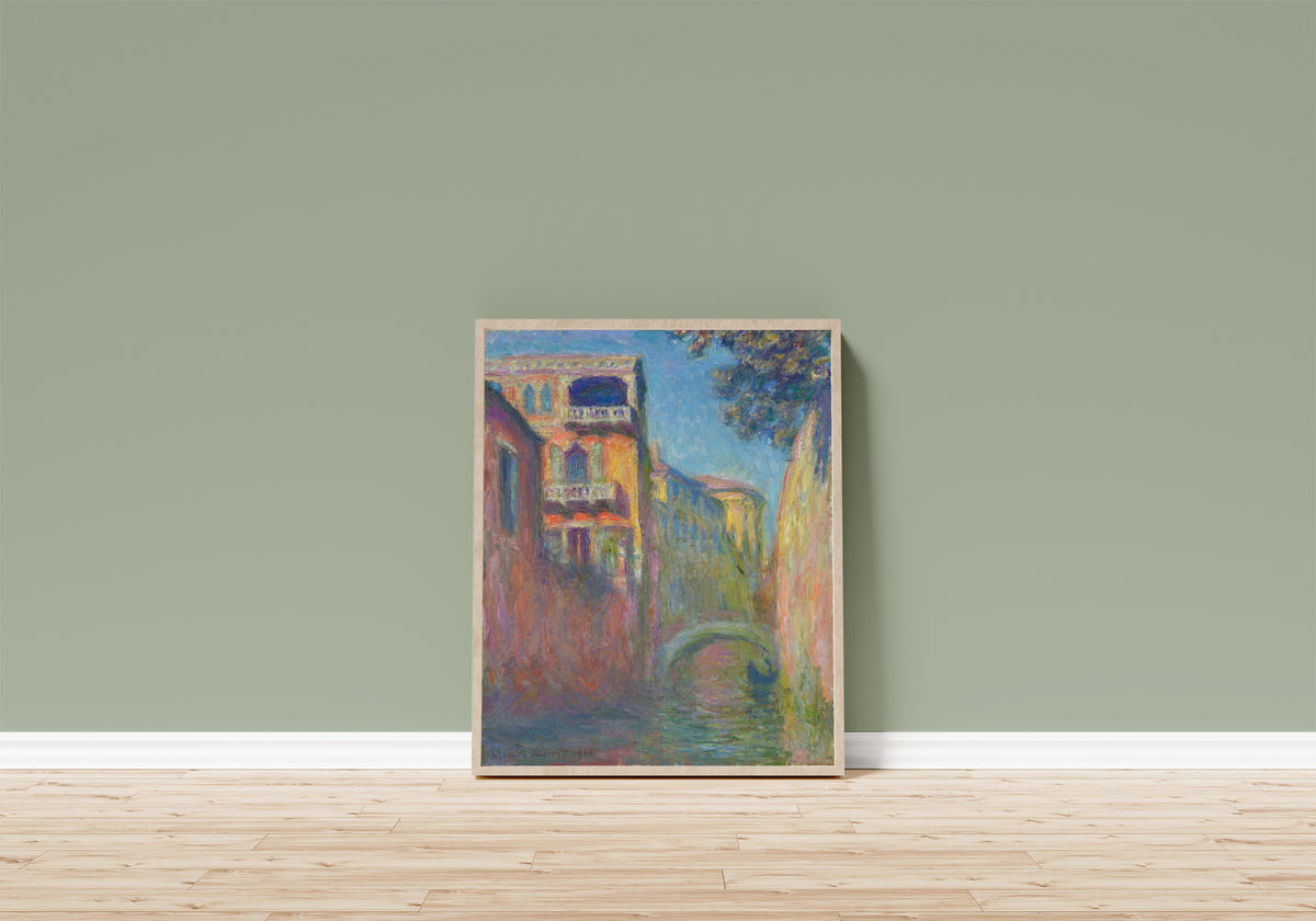 Framed art print of Rio della Salute by Claude Monet, in a light wood frame leaning on a sage green wall above a wooden floor