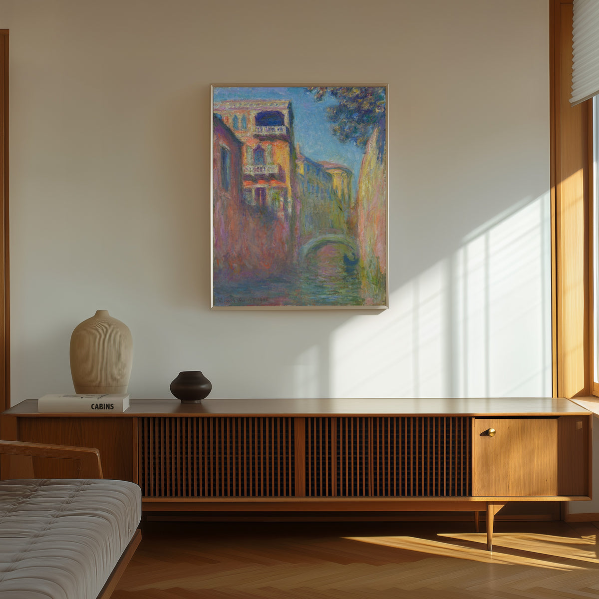 Framed art print of Rio della Salute by Claude Monet, in a thin light frame on a sunlit wall above a wooden sideboard