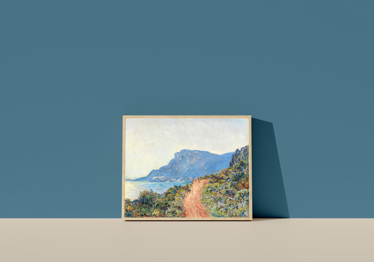 Framed art print of The Corniche near Monaco by Claude Monet, in a light wood frame leaning on a blue wall