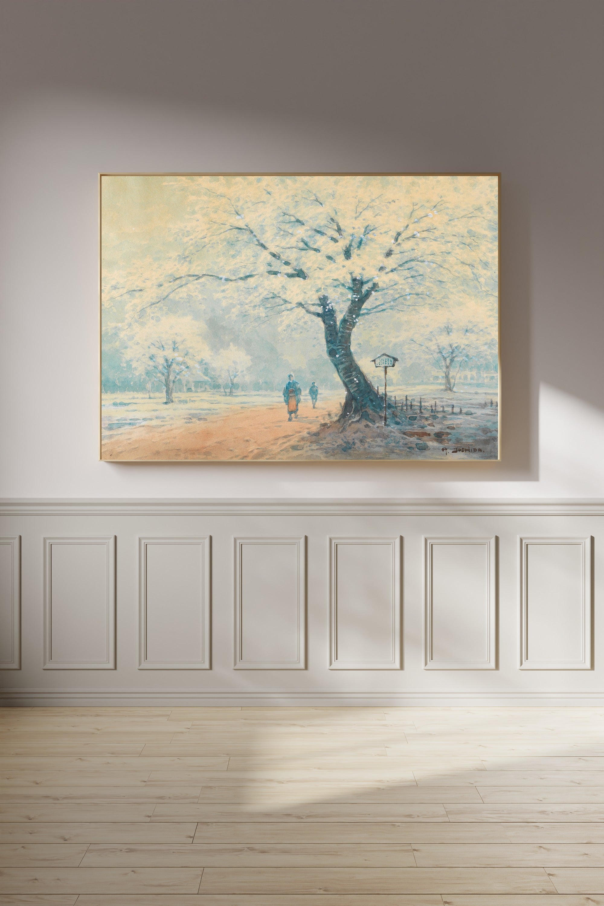 A framed landscape painting of a winter park scene with a large snow-covered tree and two small figures walking along a path, displayed on a light gray wall above white wainscoting and light wood flooring.