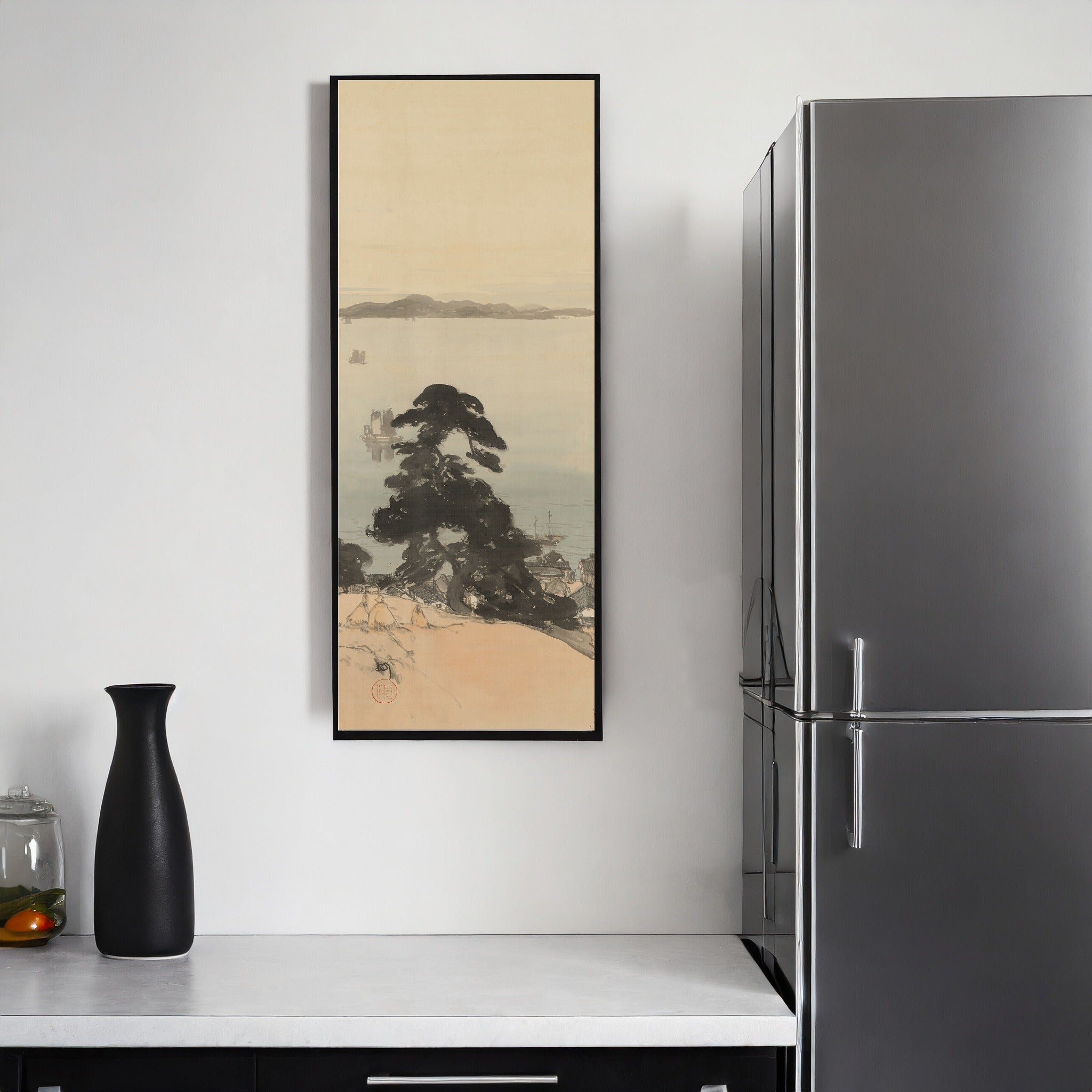 A vertical framed art print depicting a Japanese-style landscape with a dark tree, water, and pale sky, hanging on a white wall in a kitchen setting next to a stainless steel refrigerator.