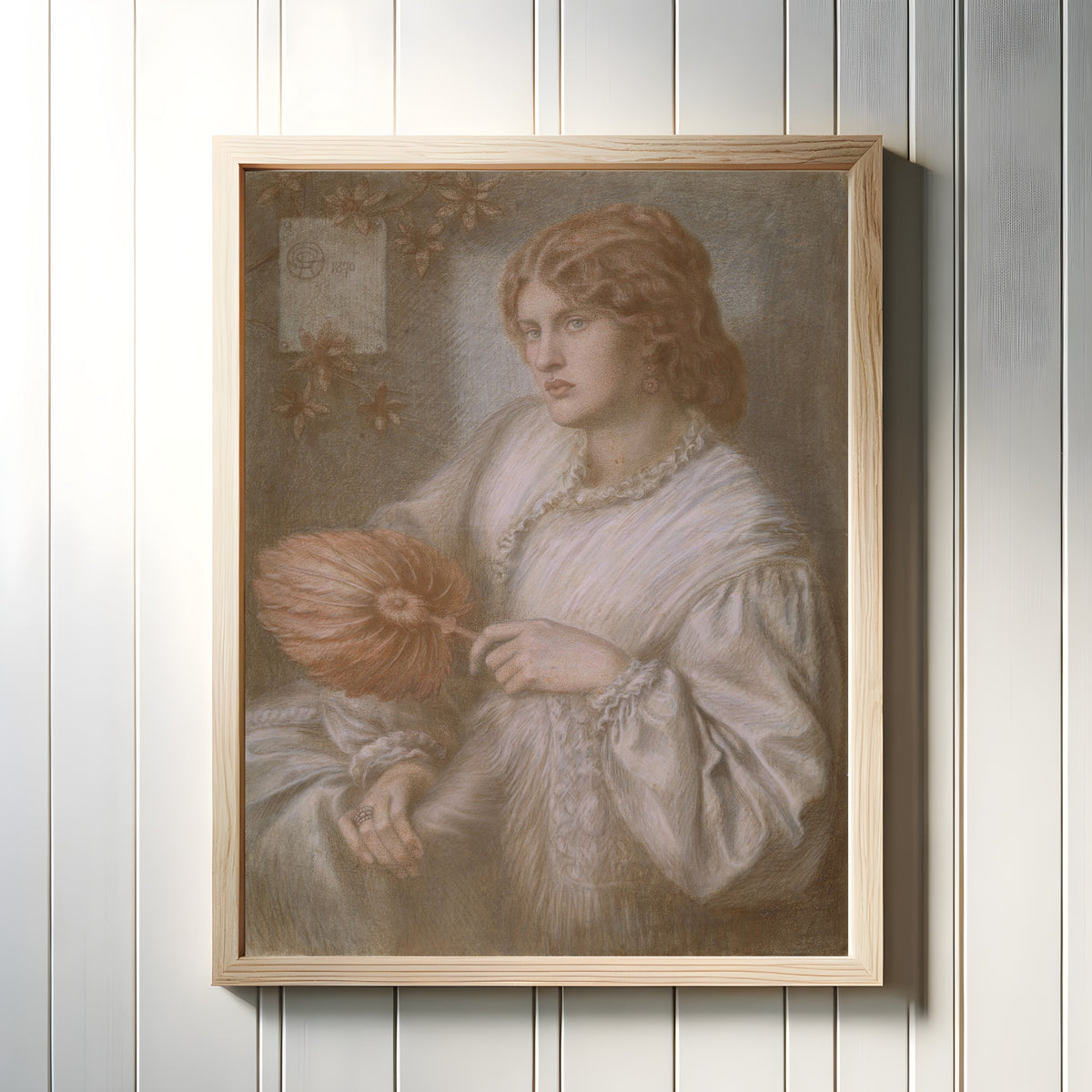 Framed art print of Portrait of Woman with a Fan by Dante Gabriel Rossetti, in a light wood frame on a white panelled wall