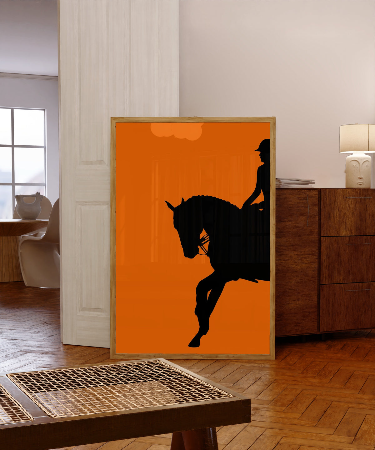 Framed art print of Horse and Rider in Orange by Vintage Poster, in a light wood frame leaning in a warm room with a parquet floor