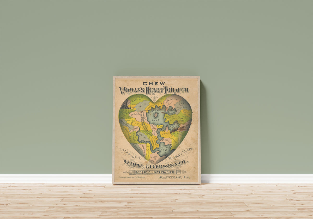 Framed art print of Map of a Woman's Heart by E.P. Beadles, in a light wood frame leaning on a sage green wall above a wooden floor