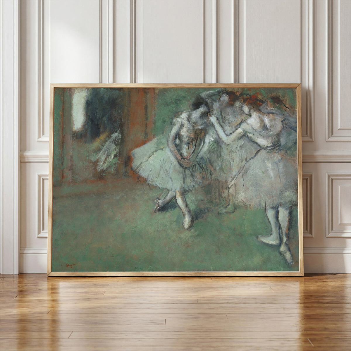 Framed art print of A Group of Dancers by Edgar Degas, in a light wood frame leaning against a panelled white wall