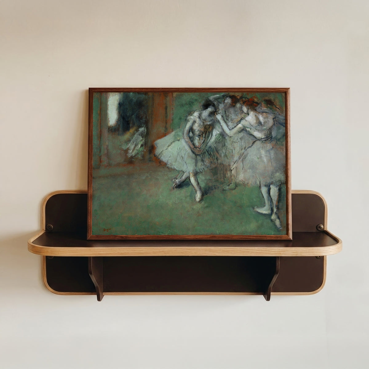 Framed art print of A Group of Dancers by Edgar Degas, in a dark wood frame resting on a wall shelf
