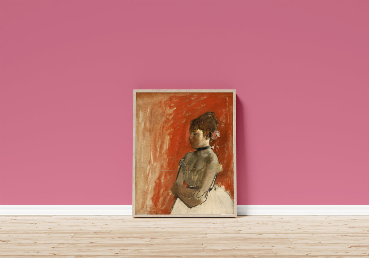 Framed art print of Ballet Dancer with Arms Crossed by Edgar Degas, in a light wood frame leaning on a pink wall above a wooden floor
