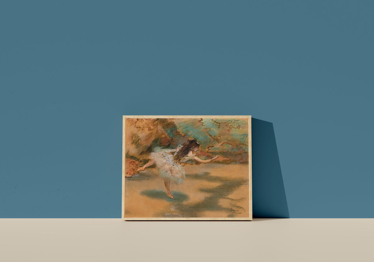 Framed art print of Dancer on Pointe by Edgar Degas, in a light wood frame leaning on a blue wall