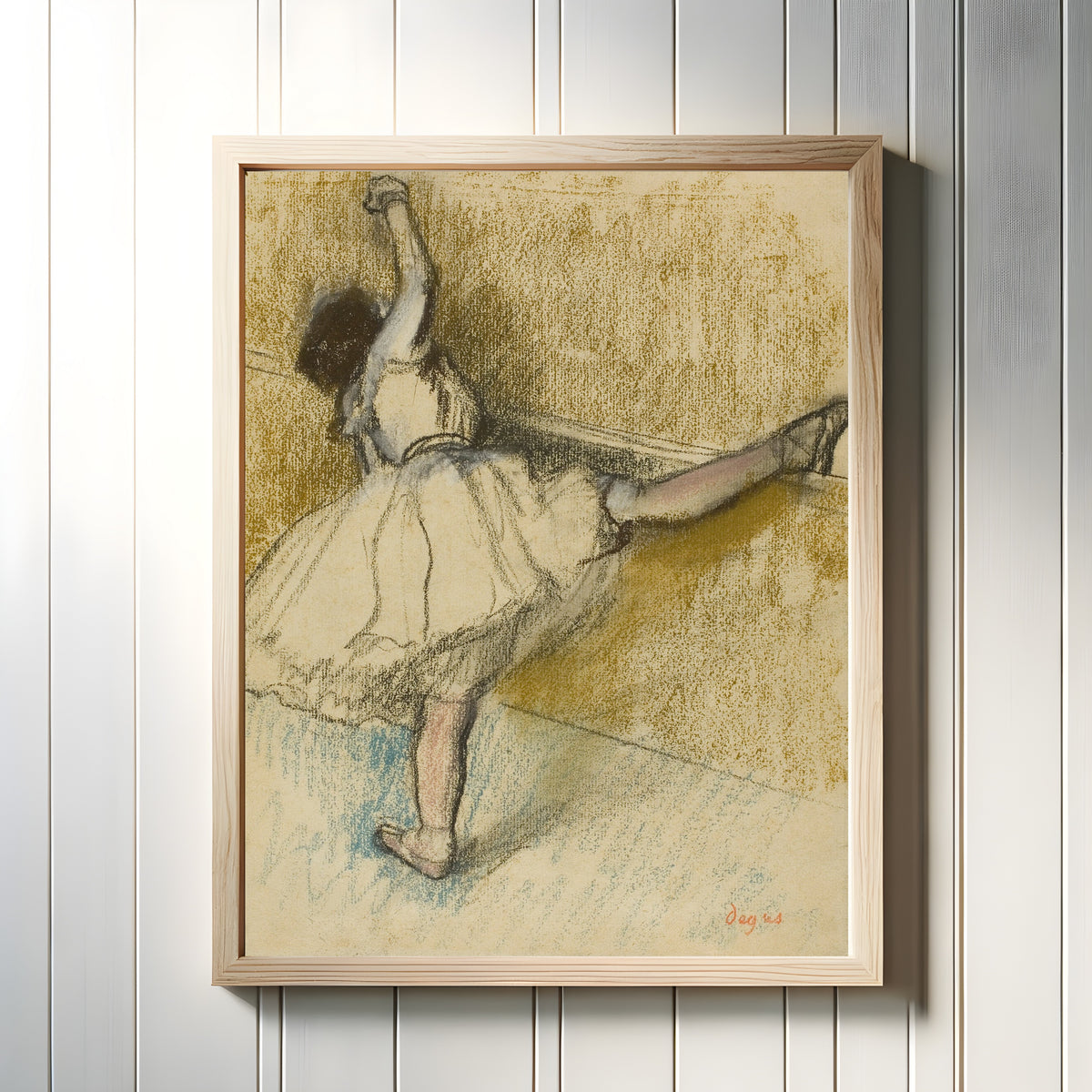 Framed art print of Dancer Stretching at the Bar by Edgar Degas, in a light wood frame on a white panelled wall