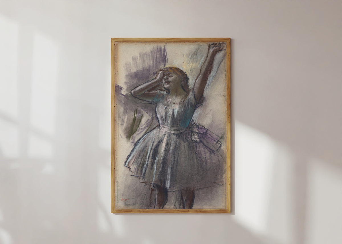 Framed art print of Dancer Stretching by Edgar Degas, in a light wood frame on a sunlit white wall
