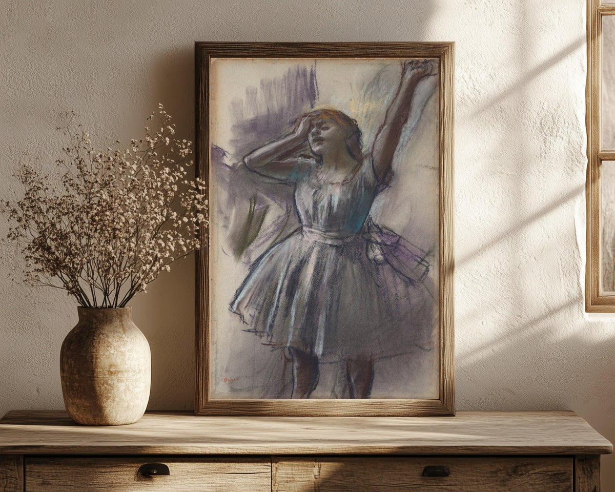 Framed art print of Dancer Stretching by Edgar Degas, in a dark wood frame leaning on a rustic console beside dried flowers