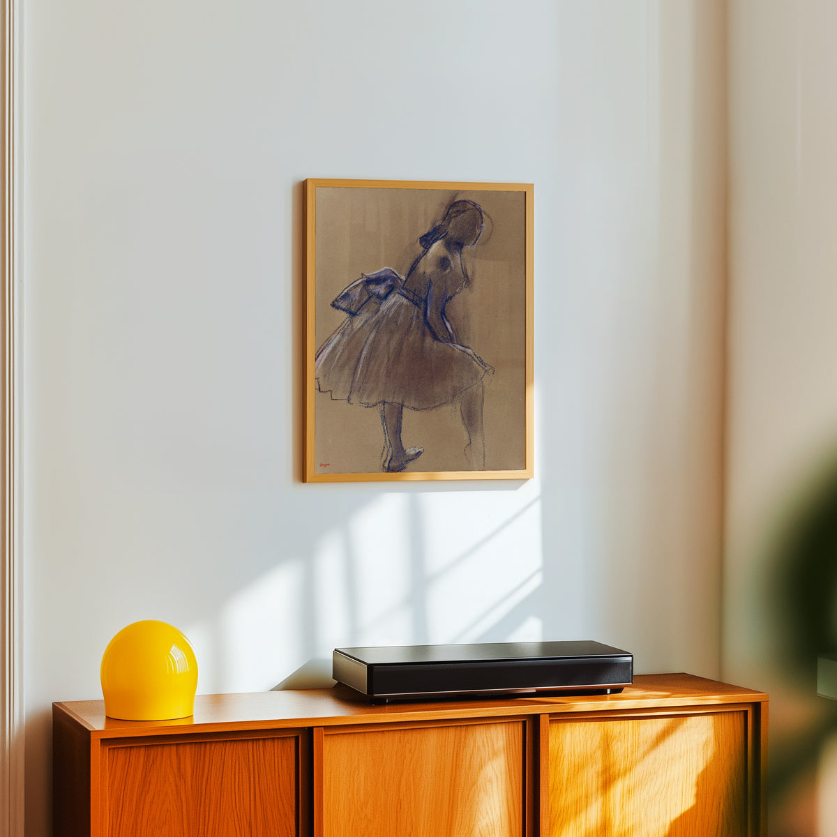 Framed art print of Danseuse debout, de profil by Edgar Degas, in a light wood frame on a white wall above an orange sideboard