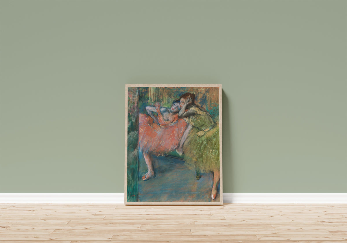 Framed art print of Danseuses au foyer by Edgar Degas, in a light wood frame leaning on a sage green wall above a wooden floor