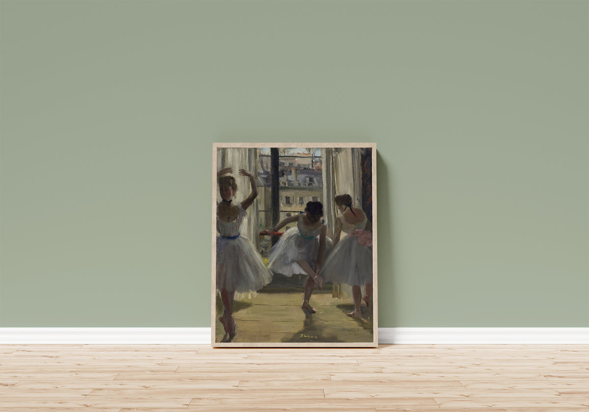 Framed art print of Danseuses dans une salle d’exercice (Trois… by Edgar Degas, in a light wood frame leaning on a sage green wall above a wooden floor