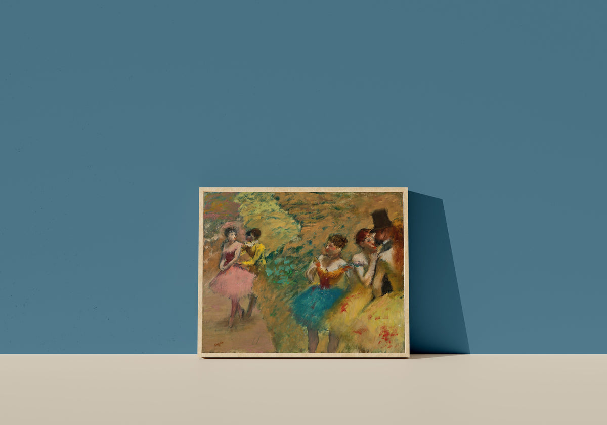 Framed art print of Danseuses (Les Coulisses de l’Opéra) by Edgar Degas, in a light wood frame leaning on a blue wall