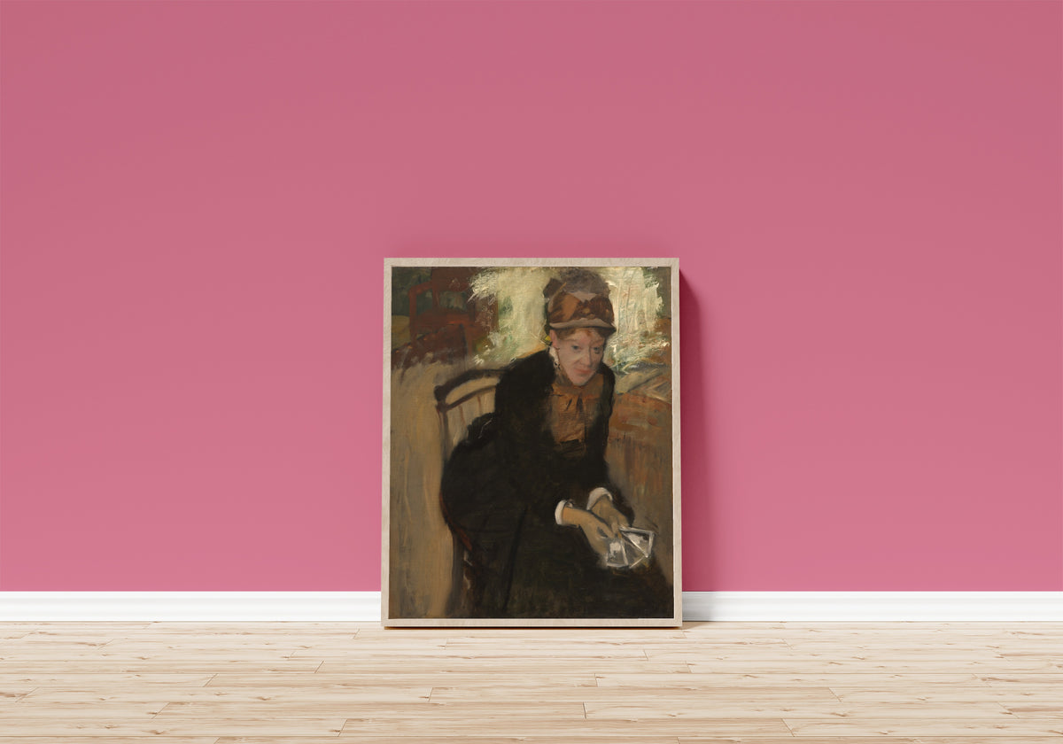 Framed art print of Mary Cassatt by Edgar Degas, in a light wood frame leaning on a pink wall above a wooden floor