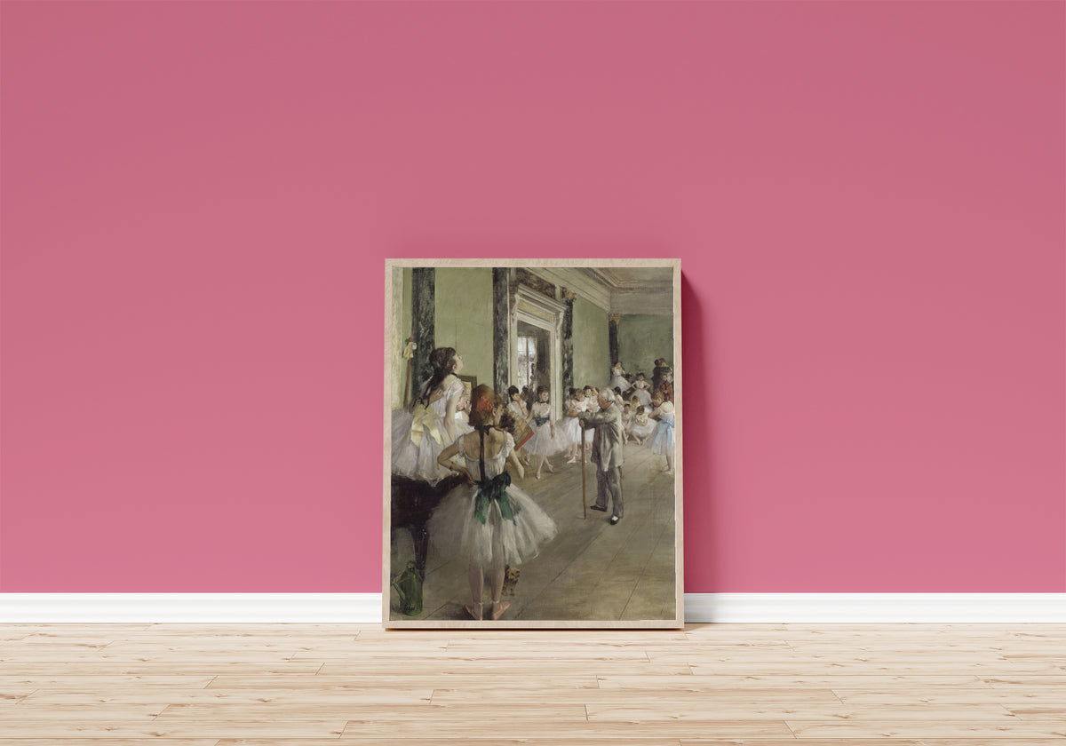 Framed art print of The Ballet Class by Edgar Degas, in a light wood frame leaning on a pink wall above a wooden floor