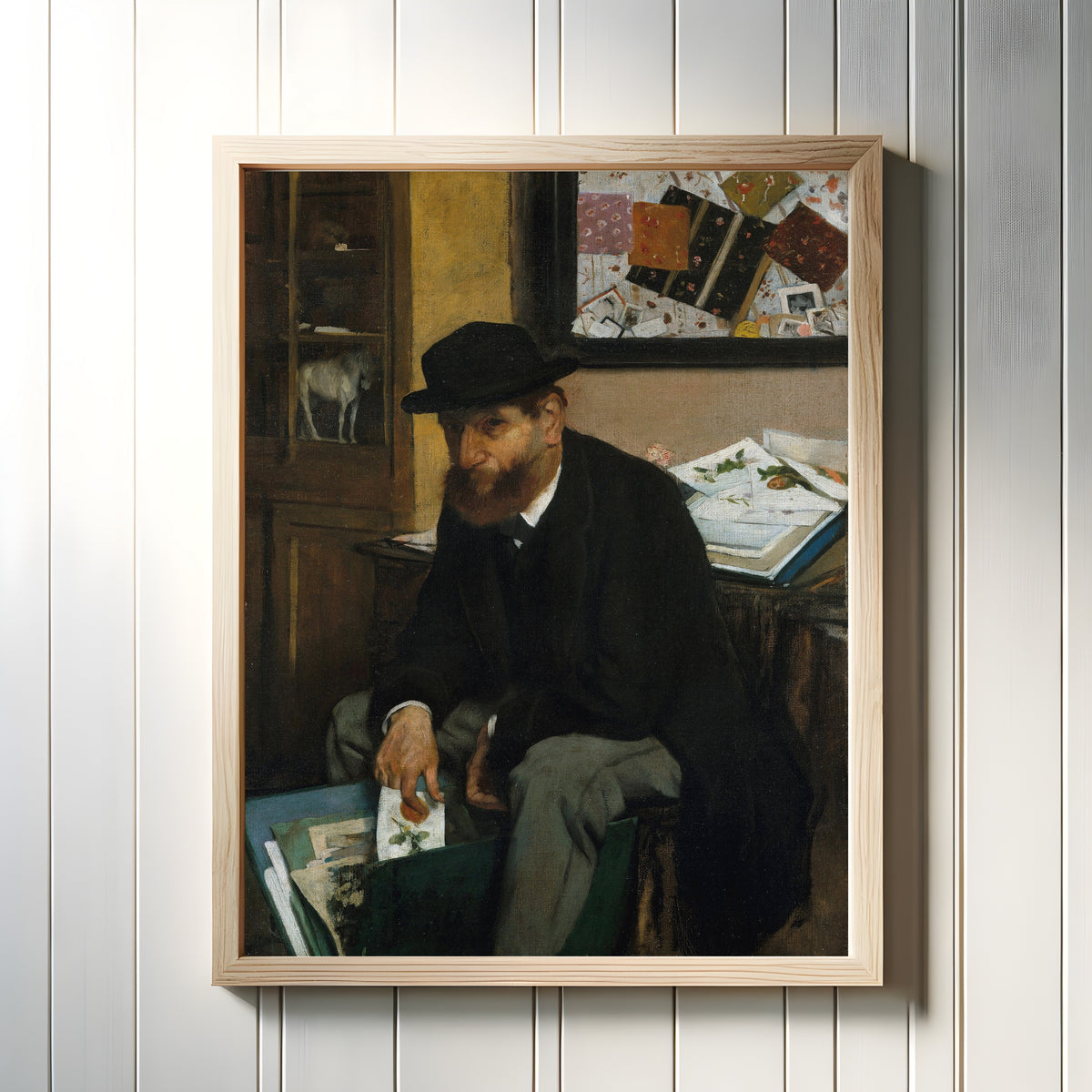 Framed art print of The Collector of Prints by Edgar Degas, in a light wood frame on a white panelled wall