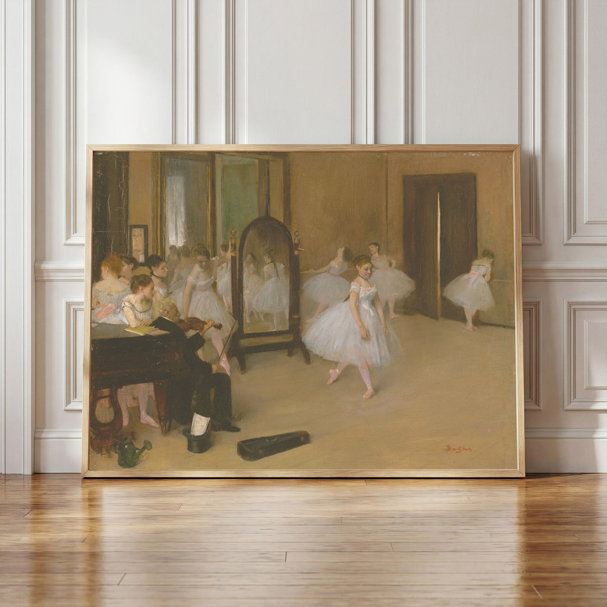 Framed art print of The Dancing Class by Edgar Degas, in a light wood frame leaning against a panelled white wall