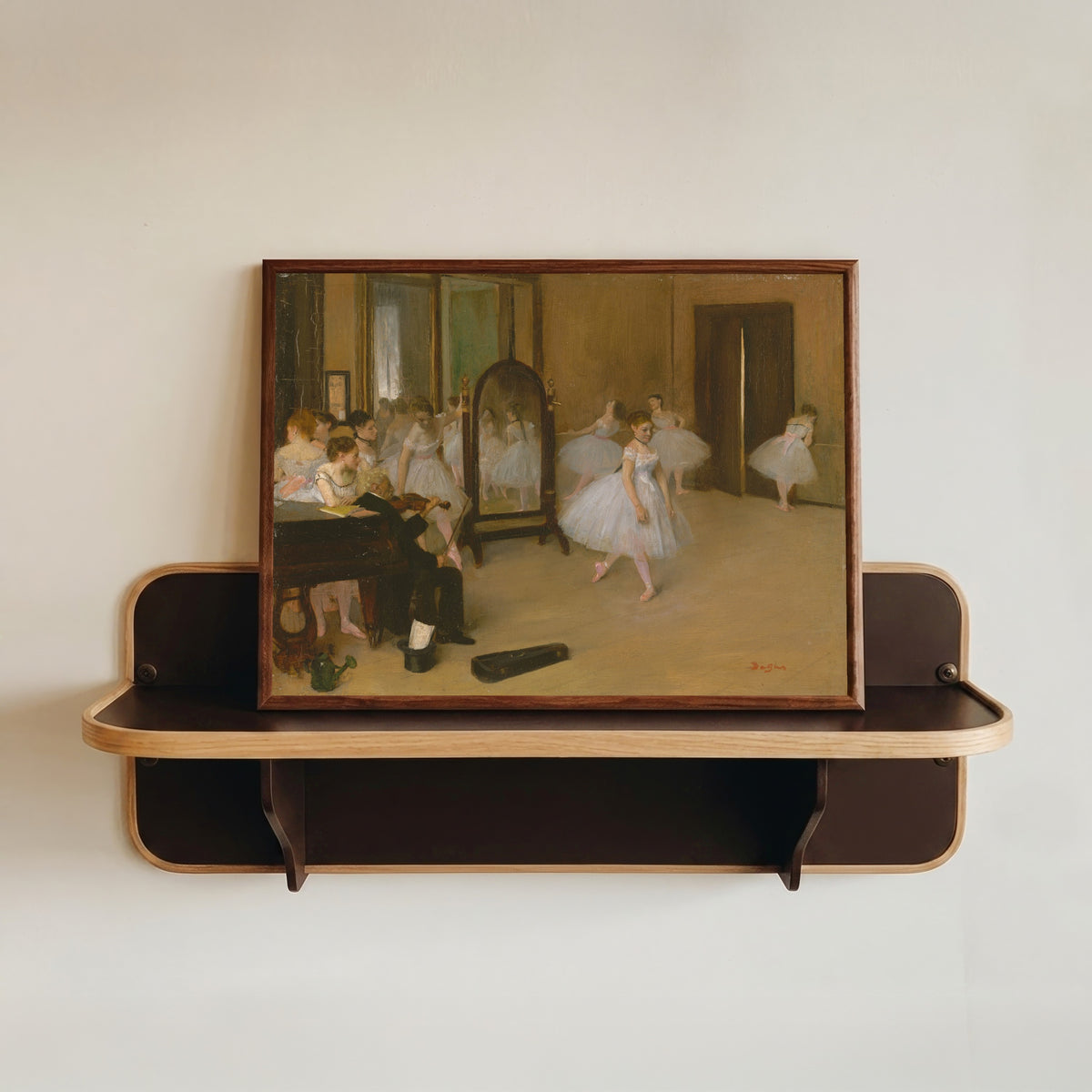Framed art print of The Dancing Class by Edgar Degas, in a dark wood frame resting on a wall shelf