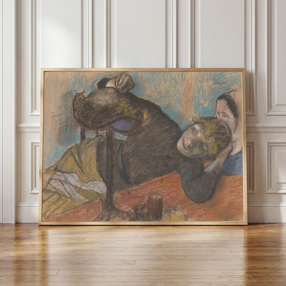 Framed art print of The Milliner by Edgar Degas, in a light wood frame leaning against a panelled white wall