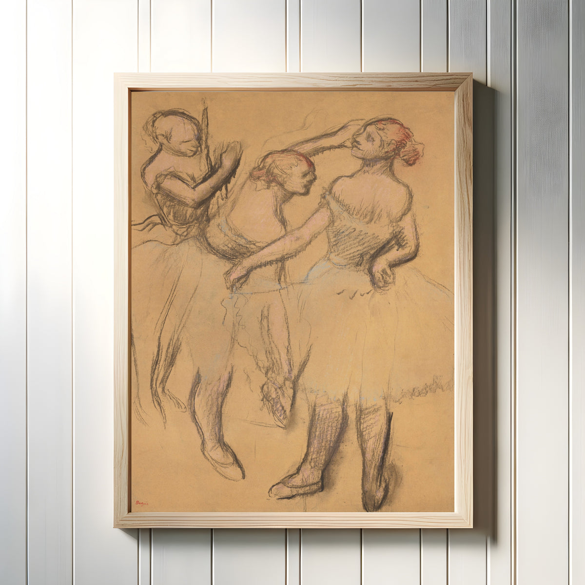 Framed art print of Trois danseuses (Dancer with Hand on Hip) by Edgar Degas, in a light wood frame on a white panelled wall