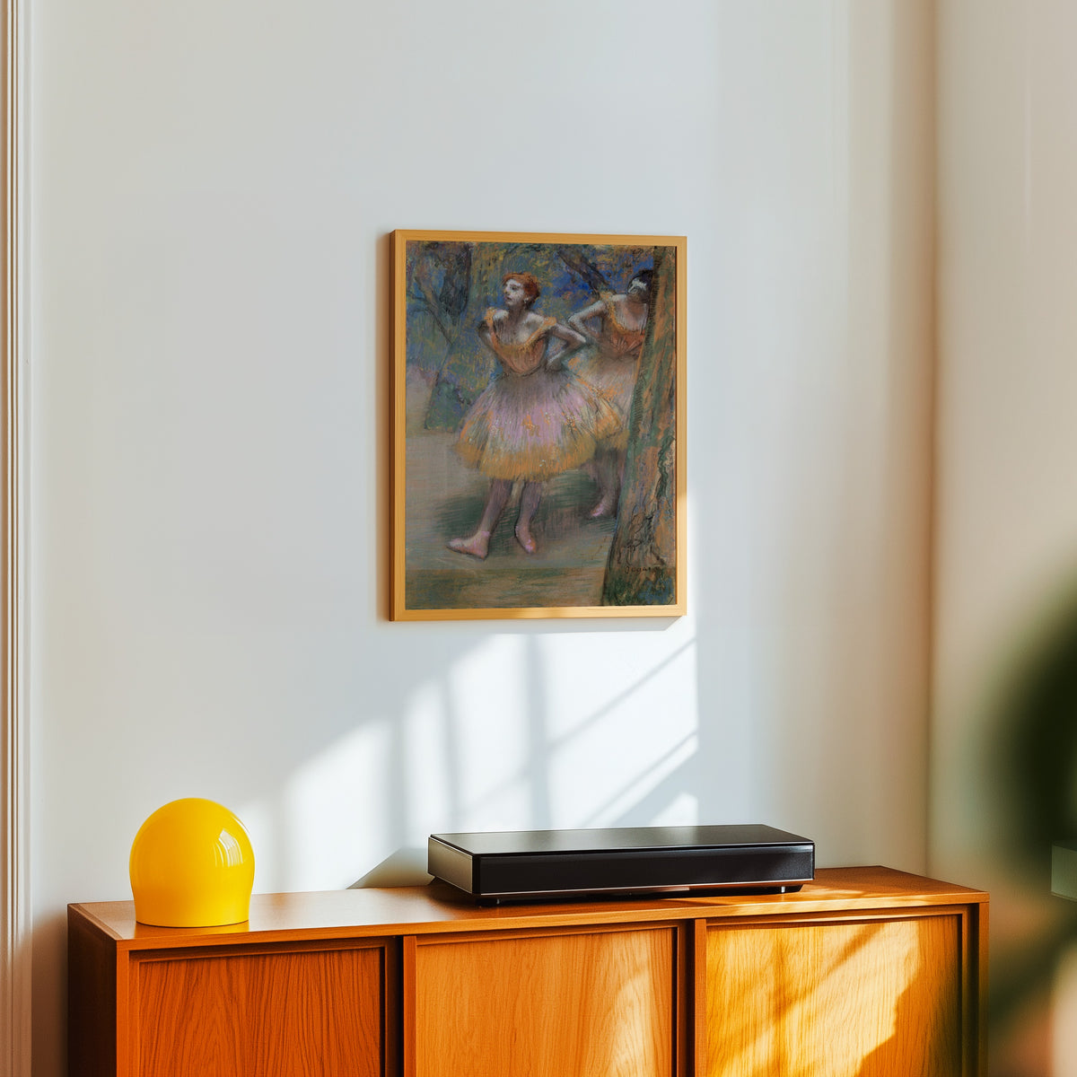 Framed art print of Two Dancers (Lilac and Orange Tutus) by Edgar Degas, in a light wood frame on a white wall above an orange sideboard