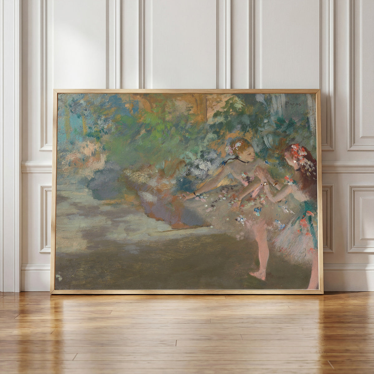 Framed art print of Two Dancers on Stage (Painted Foliage) by Edgar Degas, in a light wood frame leaning against a panelled white wall