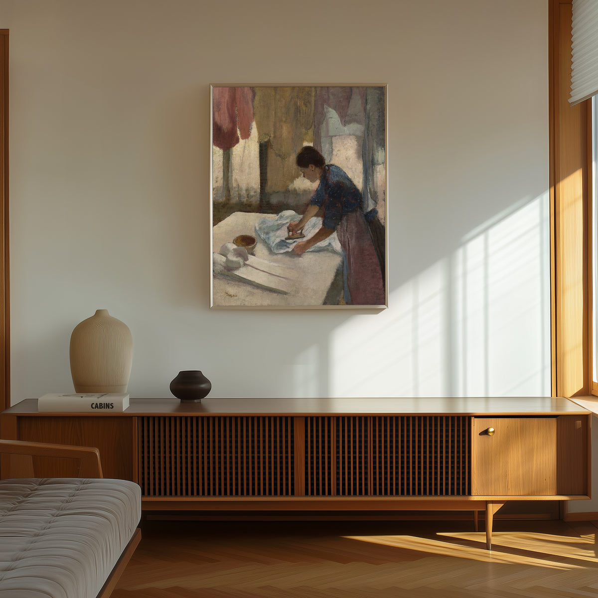 Framed art print of Woman Ironing in a Blue Blouse by Edgar Degas, in a thin light frame on a sunlit wall above a wooden sideboard