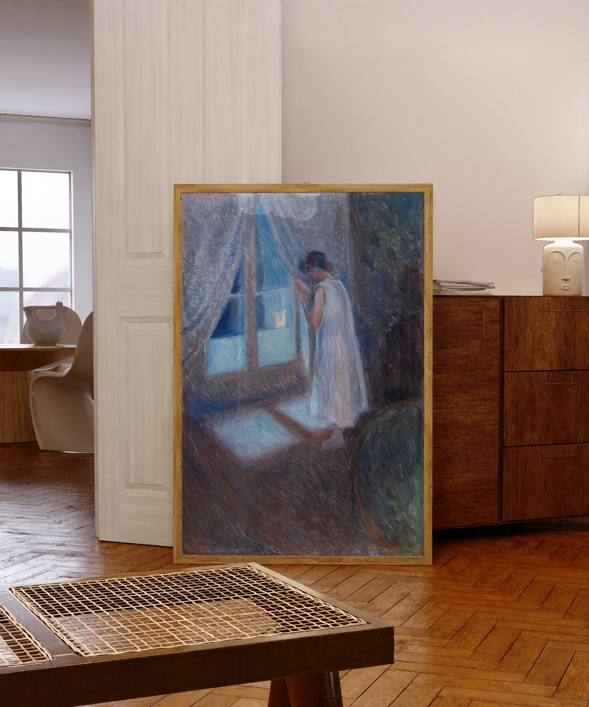 Framed art print of The Girl by the Window by Edvard Munch, in a light wood frame leaning in a warm room with a parquet floor