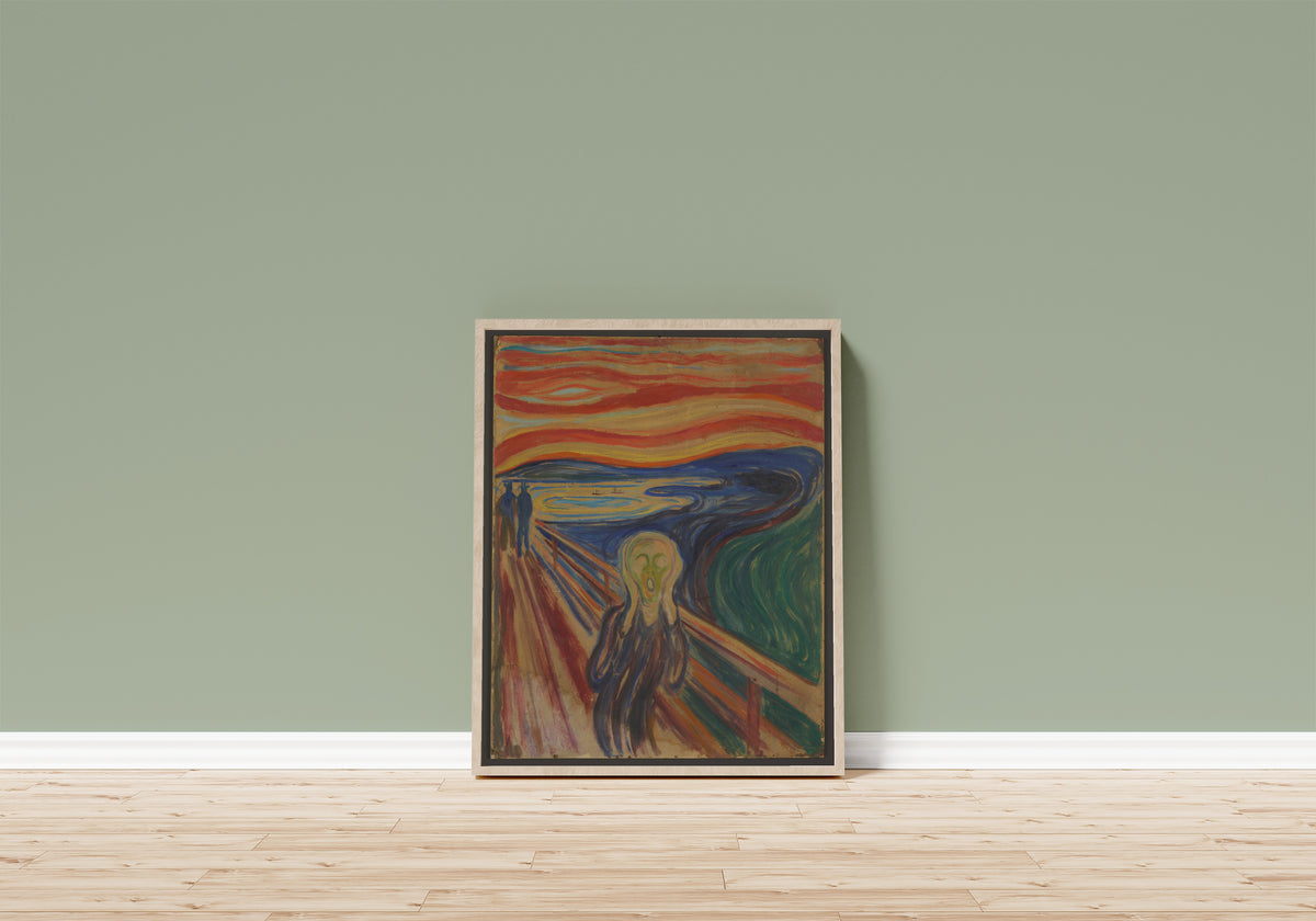 Framed art print of The Scream by Edvard Munch, in a light wood frame leaning on a sage green wall above a wooden floor