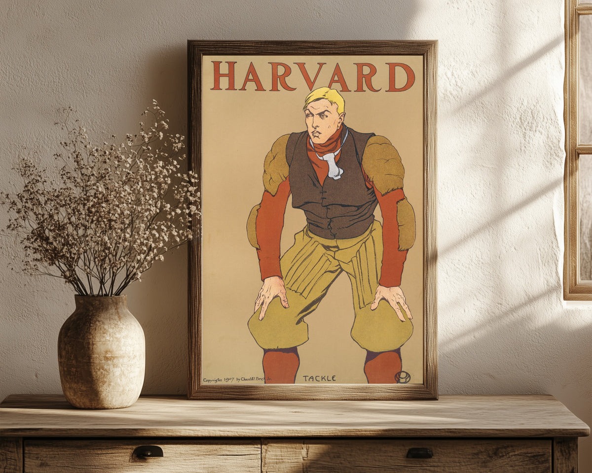Framed art print of Harvard by Edward Penfield, in a dark wood frame leaning on a rustic console beside dried flowers