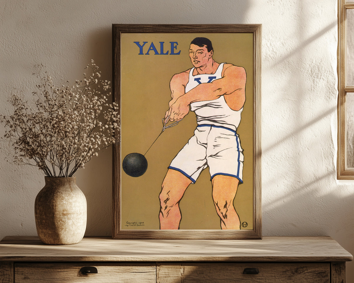 Framed art print of Yale by Edward Penfield, in a dark wood frame leaning on a rustic console beside dried flowers