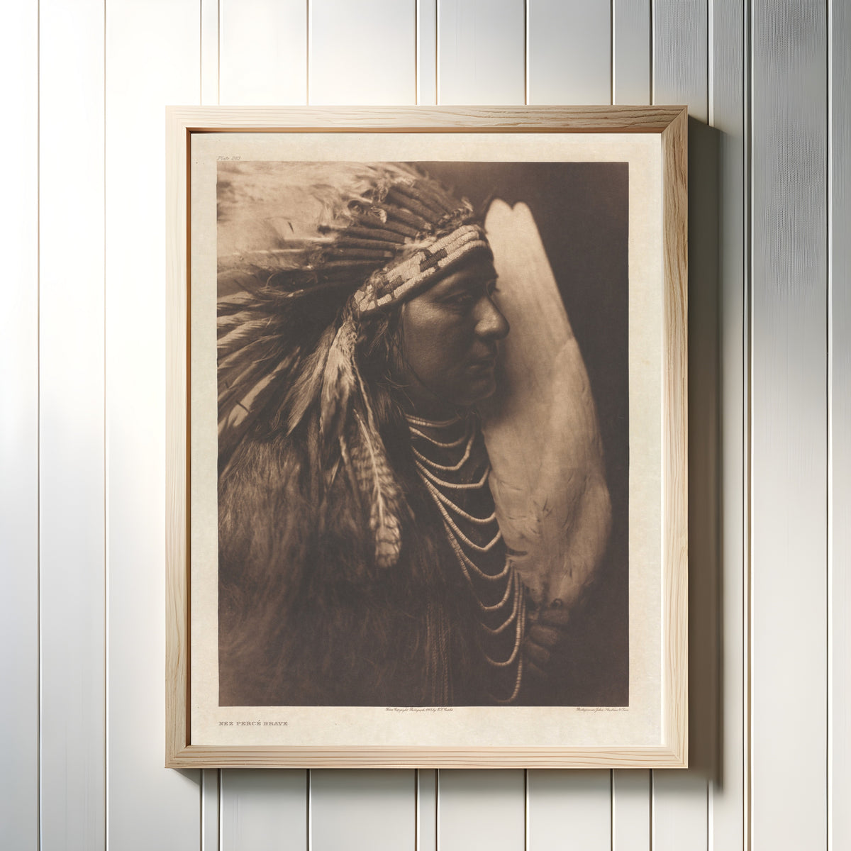 Framed art print of Nez Percé Brave by Edward S. Curtis, in a light wood frame on a white panelled wall