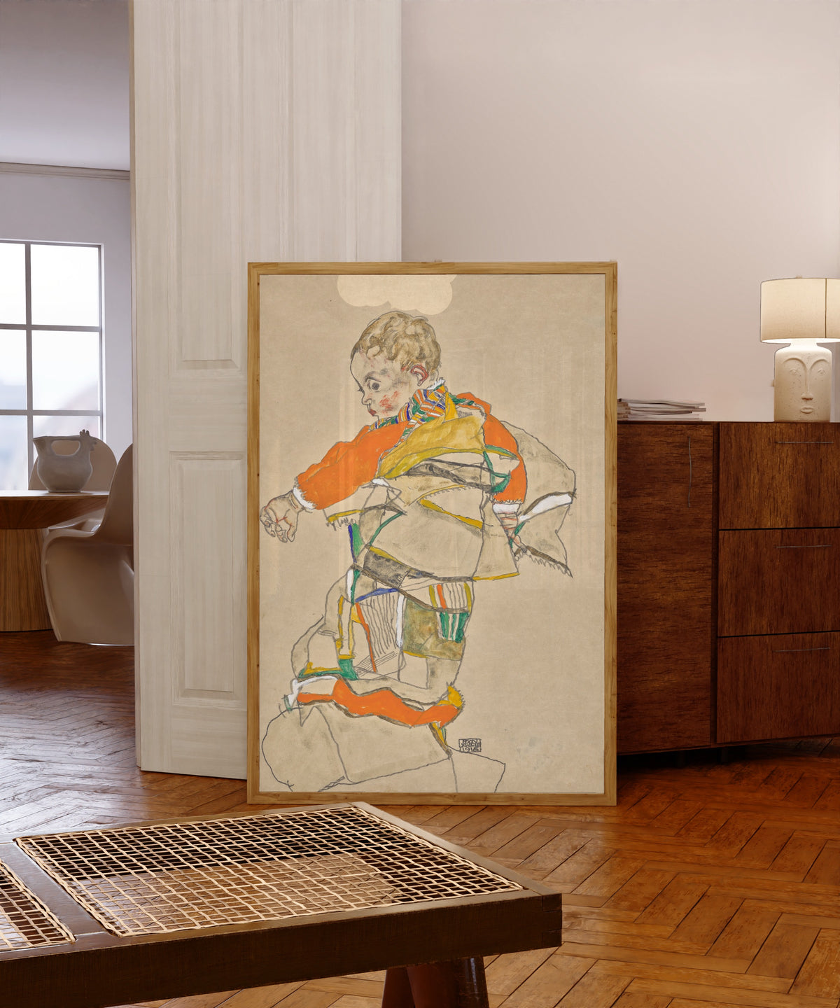 Framed art print of Portrait of a Child (Anton Peschka Jr.) by Egon Schiele, in a light wood frame leaning in a warm room with a parquet floor